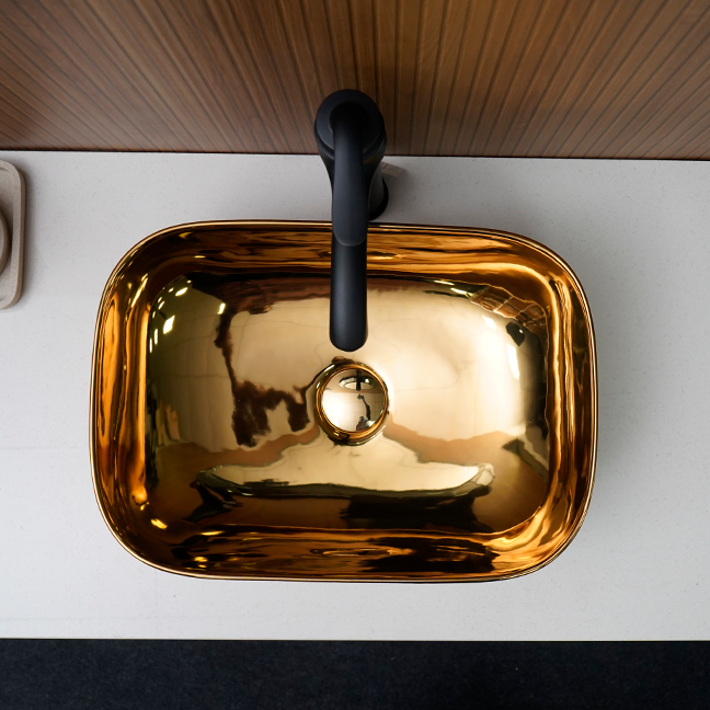 Gold sink with black faucet on a white countertop