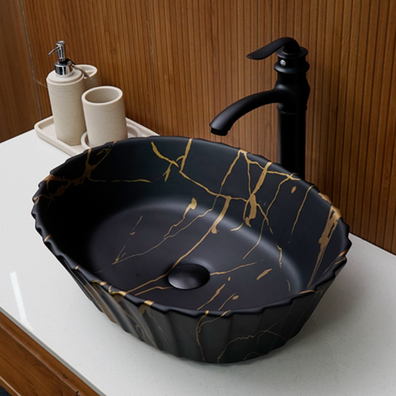 Black ceramic sink with gold accents on a white countertop, featuring a black faucet.