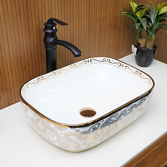 Ceramic sink with decorative patterns on a white countertop, black faucet, and plant in the background.