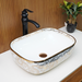 Ceramic sink with decorative patterns on a white countertop, black faucet, and plant in the background.