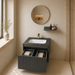 Bassino dark grey wall-mounted bathroom vanity set with fluted cabinet, white inset basin, dark stone countertop, round mirror and utility shelf in a modern luxury bathroom.  