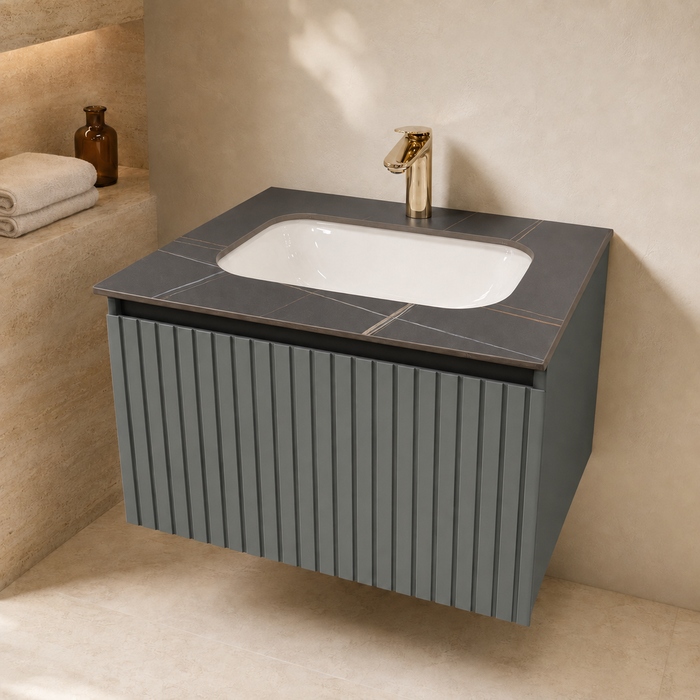 Bassino dark grey wall-mounted bathroom vanity set with fluted cabinet, white inset basin, dark stone countertop, round mirror and utility shelf in a modern luxury bathroom.  