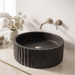 Black artificial stone table top wash basin with matte speckled finish, round shape and vertical fluted exterior, 390 × 390 × 150 mm.