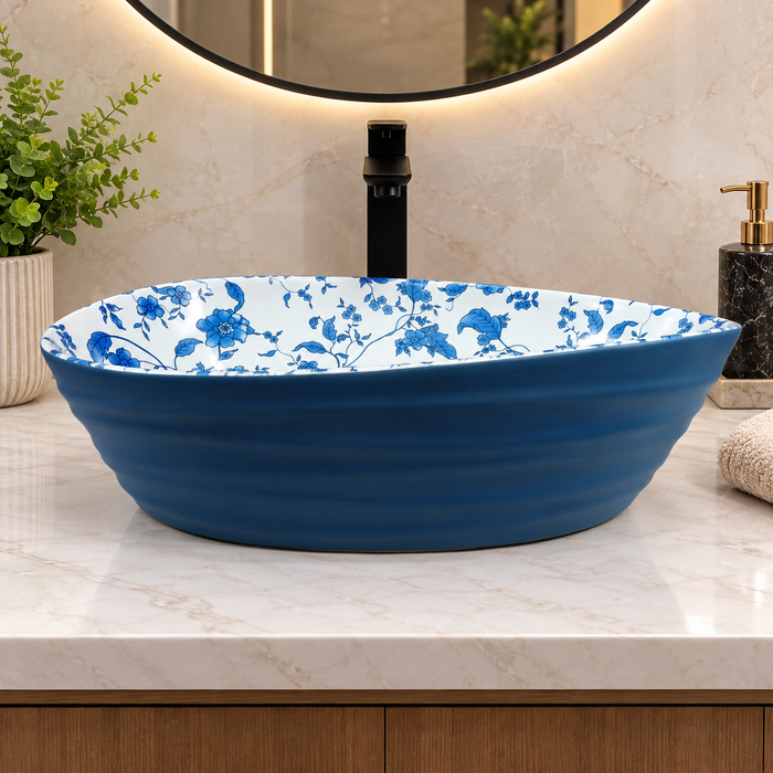 Blue and white floral ceramic table top wash basin with glossy finish, oval designer countertop basin measuring 555 × 355 × 170 mm for modern bathrooms.