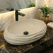 Bathroom vanity with a stone sink and black faucet, featuring a marble wall and decorative elements.