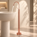 Glossy Rose gold floor mount basin faucet with tall curved spout and single lever handle, modern freestanding bathroom tap for luxury wash basin installations by Bassino.