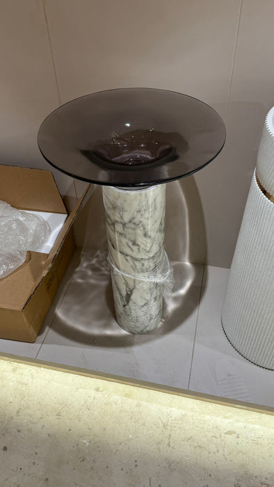 Modern side table with a glass top and marble base on a tiled floor.