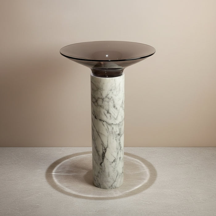 Modern side table with a glass top and marble base on a tiled floor.