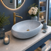 Light blue Ceramic finish oval table top wash basin, 600x400x150 mm, displayed in a modern luxury bathroom setting.