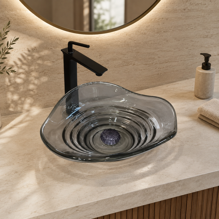 Smoky transparent glass table top wash basin with sculpted concentric design, matching glass waste coupling ball and 450 × 320 × 130 mm dimensions.