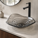 Smoky transparent glass table top wash basin with sculpted concentric design, matching glass waste coupling ball and 450 × 320 × 130 mm dimensions.