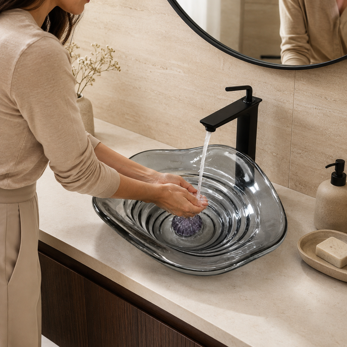 Smoky transparent glass table top wash basin with sculpted concentric design, matching glass waste coupling ball and 450 × 320 × 130 mm dimensions.