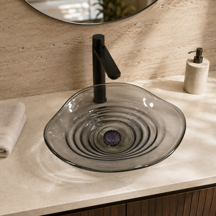 Smoky transparent glass table top wash basin with sculpted concentric design, matching glass waste coupling ball and 450 × 320 × 130 mm dimensions.