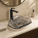 Smoky transparent glass table top wash basin with sculpted concentric design, matching glass waste coupling ball and 450 × 320 × 130 mm dimensions.